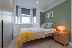 Ein Schlafzimmer mit Bett, Nachttisch und einem Fenster mit Jalousien.