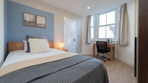 A bedroom with a bed, bedside table, lamp, desk, chair, and a window with curtains. - Lovely 1-bedroom apartment in welcoming Epsom for your stay (Epsom)