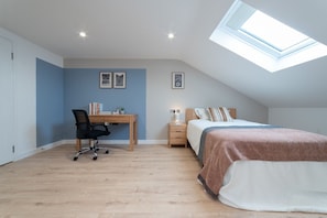 Ein Schlafzimmer mit Oberlicht, Schreibtisch, Stuhl, Bett und zwei Nachttischen.