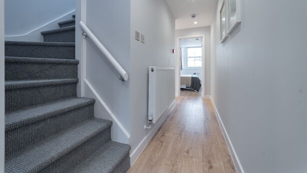 A hallway with a carpeted staircase, a radiator, and a bed in the background. - Lovely 1-bedroom apartment in welcoming Epsom for your stay (Epsom)