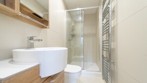 A modern bathroom with a white sink, toilet, and glass shower enclosure. - Lovely 1-bedroom apartment in welcoming Epsom for your stay (Epsom)