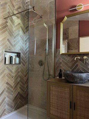 Une salle de bain moderne avec un pare-chocs en carreaux disposés en chevron, une douche à parois de verre, un meuble-lavabo en bois et un grand miroir.