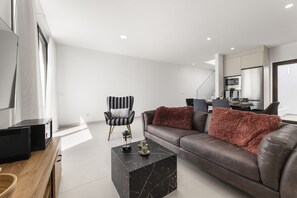A modern living room with a sofa, a coffee table, a TV, and a kitchen area in the background. - Villa Infinity Views 3 by Escape Home (Tahiche)
