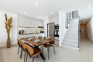 A modern kitchen with white cabinets, a dining table set with plates and glasses, and a staircase with a glass railing. - Villa Infinity Views 4 by Escape Home (Tahiche)