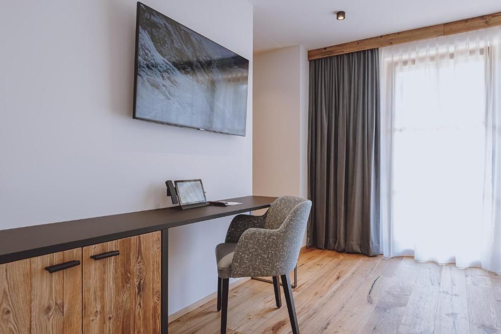 Una habitación moderna con un escritorio de madera, una silla, un televisor de pantalla plana y un ventanal con cortinas.