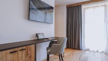 Una habitación moderna con un escritorio de madera, una silla, un televisor de pantalla plana y un ventanal con cortinas.