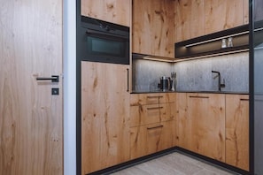 A modern kitchen with wooden cabinetry, a built-in oven, and a stainless steel countertop. - Zaglgut (Kaprun)