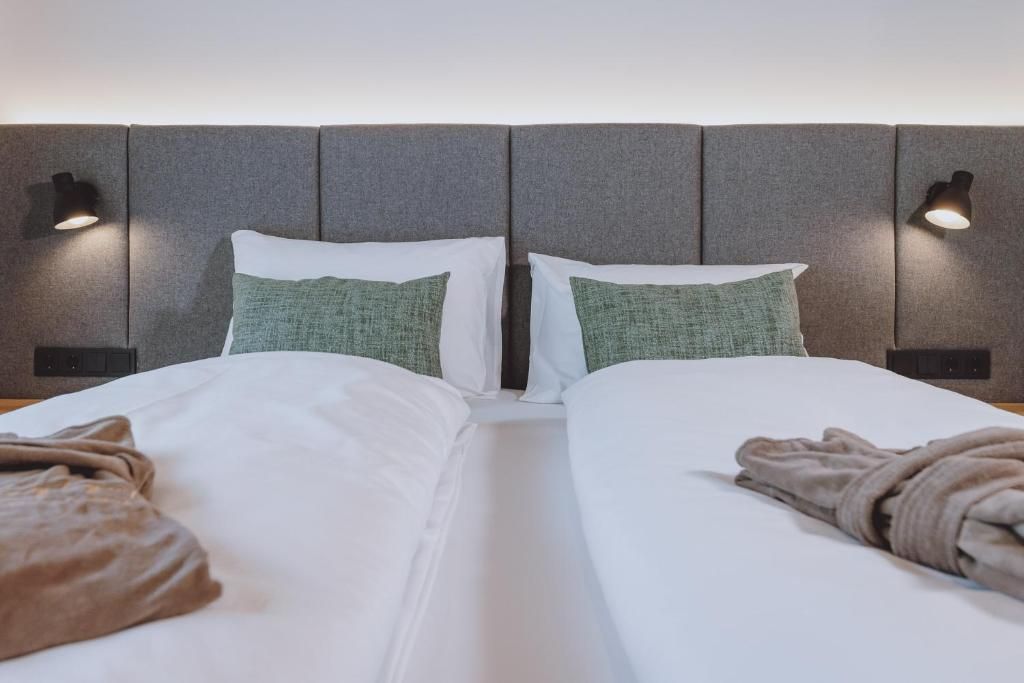 Una cama doble con sábanas blancas, dos almohadas y una manta.