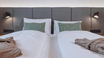 Una cama doble con sábanas blancas, dos almohadas y una manta.