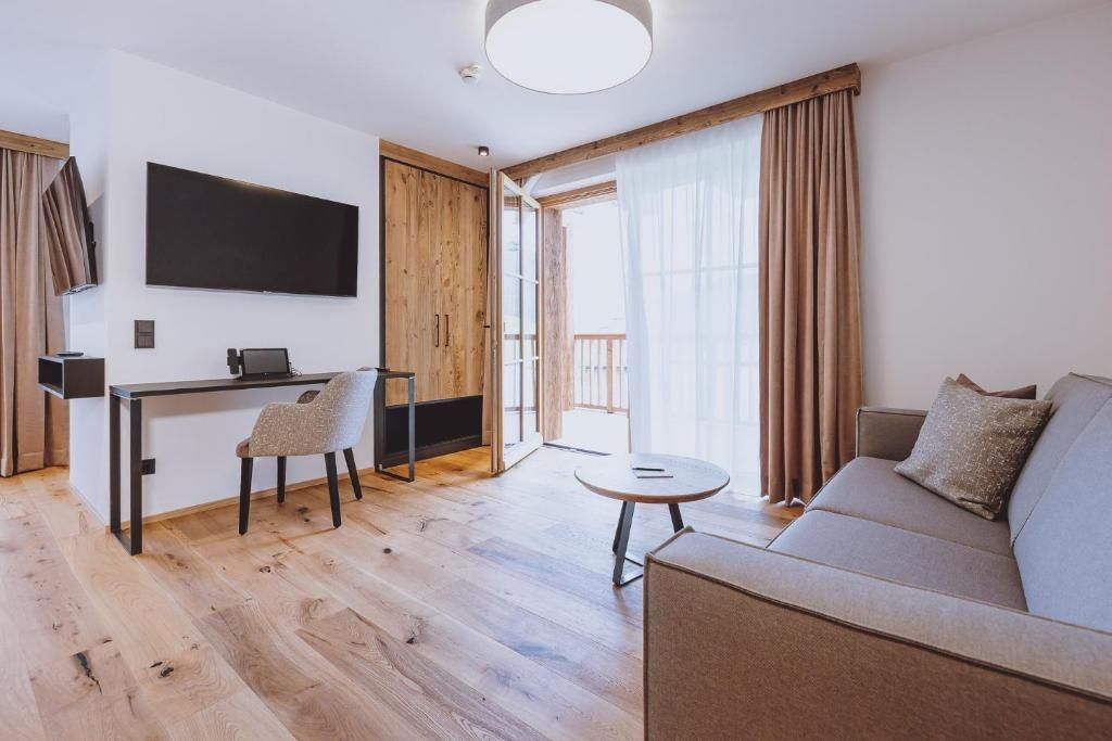 Una sala de estar moderna con un sofá, un comedor con sillas, un televisor montado en la pared y un ventanal con cortinas.