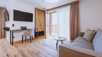 Una sala de estar moderna con un sofá, un comedor con sillas, un televisor montado en la pared y un ventanal con cortinas.