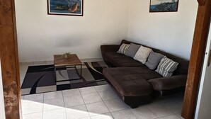 A living room with a sectional sofa, a small table with a plant, and two framed pictures on the walls.