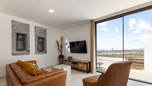 Una sala de estar moderna con un sofá de cuero, un sillón marrón, un televisor de pantalla plana y obras de arte en la pared.