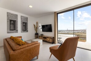 Un salon moderne avec un canapé en cuir, un fauteuil marron, un téléviseur à écran plat et des œuvres d’art accrochées au mur.