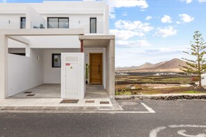 Ein modernes Gebäude mit weißer Fassade, einer Holztür und Blick auf eine gebirgige Landschaft.