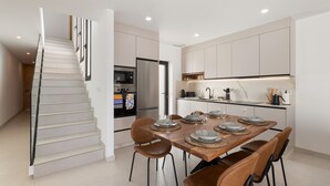 Una cocina moderna con comedor, que incluye una escalera, electrodomésticos de acero inoxidable y una mesa de madera.