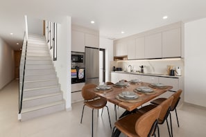 Eine moderne Küche mit Essbereich, inklusive Treppe, Edelstahlgeräten und einem Holztisch.