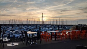 A marina with boats docked, outdoor tables and chairs, and a sunset in the background. - House Port Bourgenay 6-8 pers - 3 bdrms - pools/toboggans-Plage-Golf- Activities (Talmont-Saint-Hilaire)