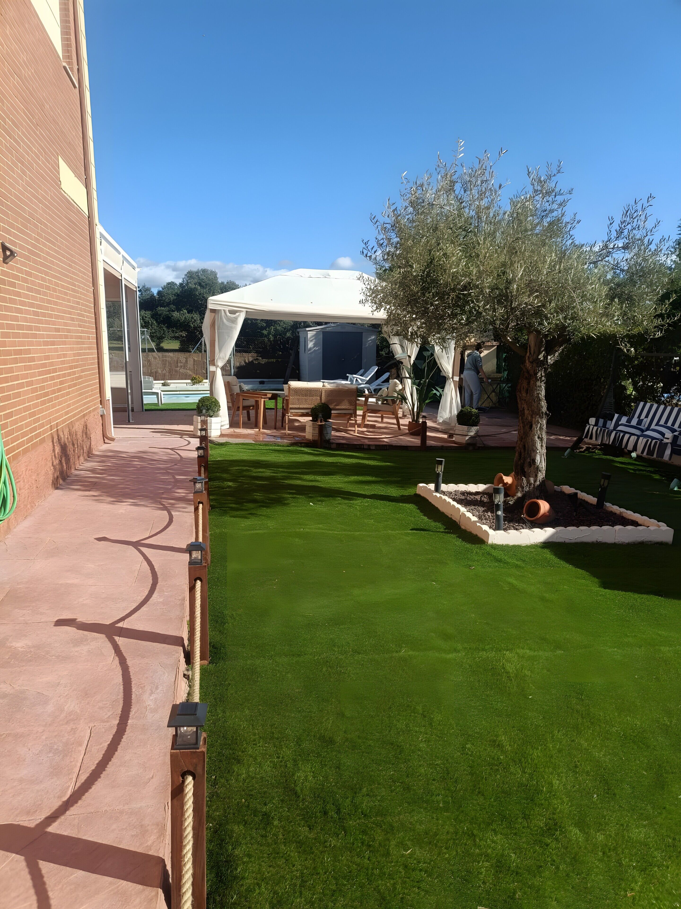 Un patio con una carpa blanca, mobiliario exterior, un árbol y un muro de ladrillo.