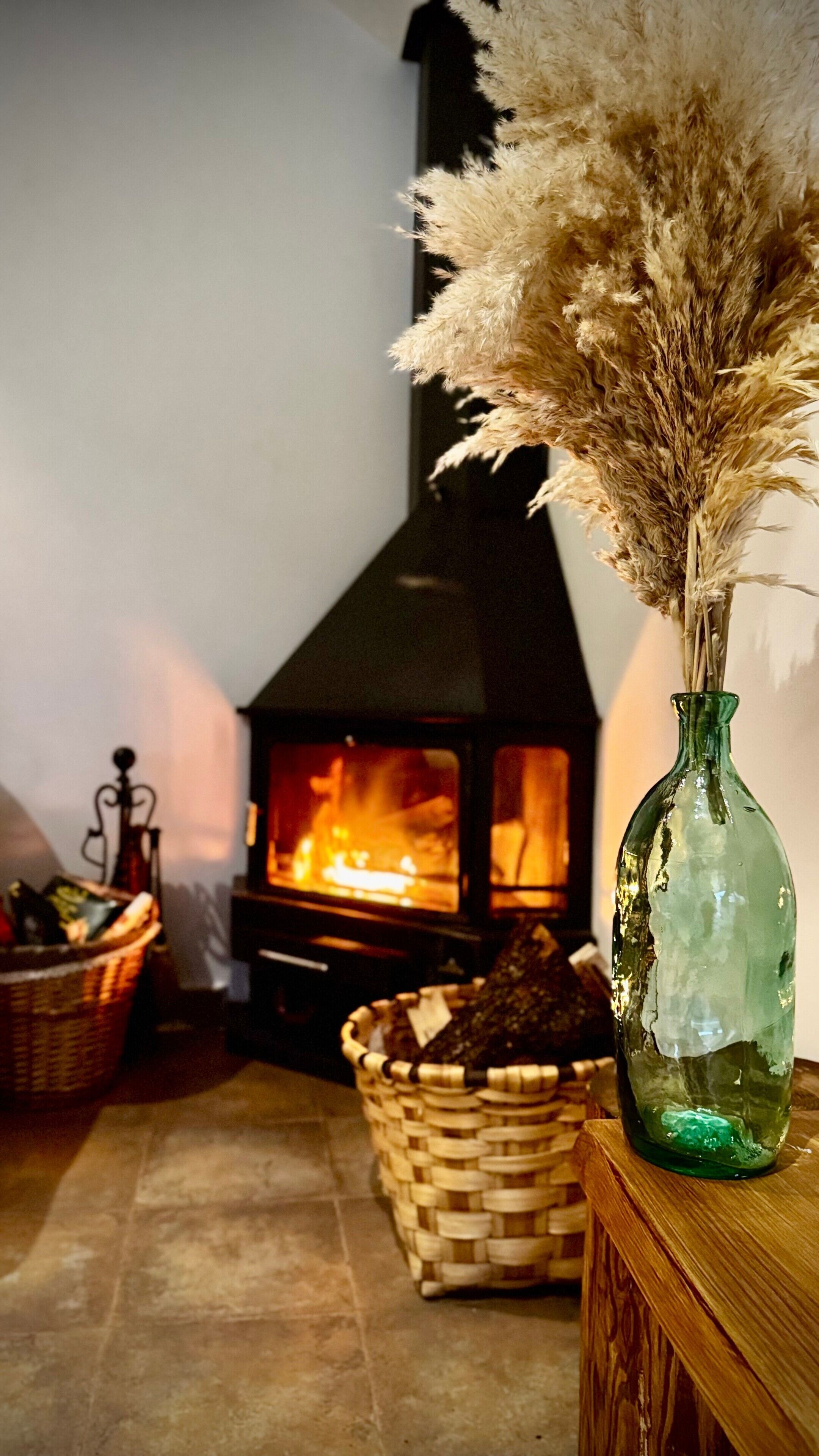 A room with a fireplace, a wicker basket, and a green vase with dried pampas grass.