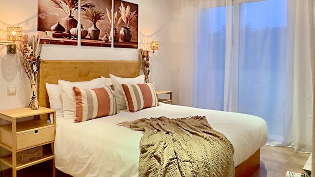 Una camera da letto con un letto grande, una testiera in legno, un comodino, una lampada a parete e una finestra con tende.