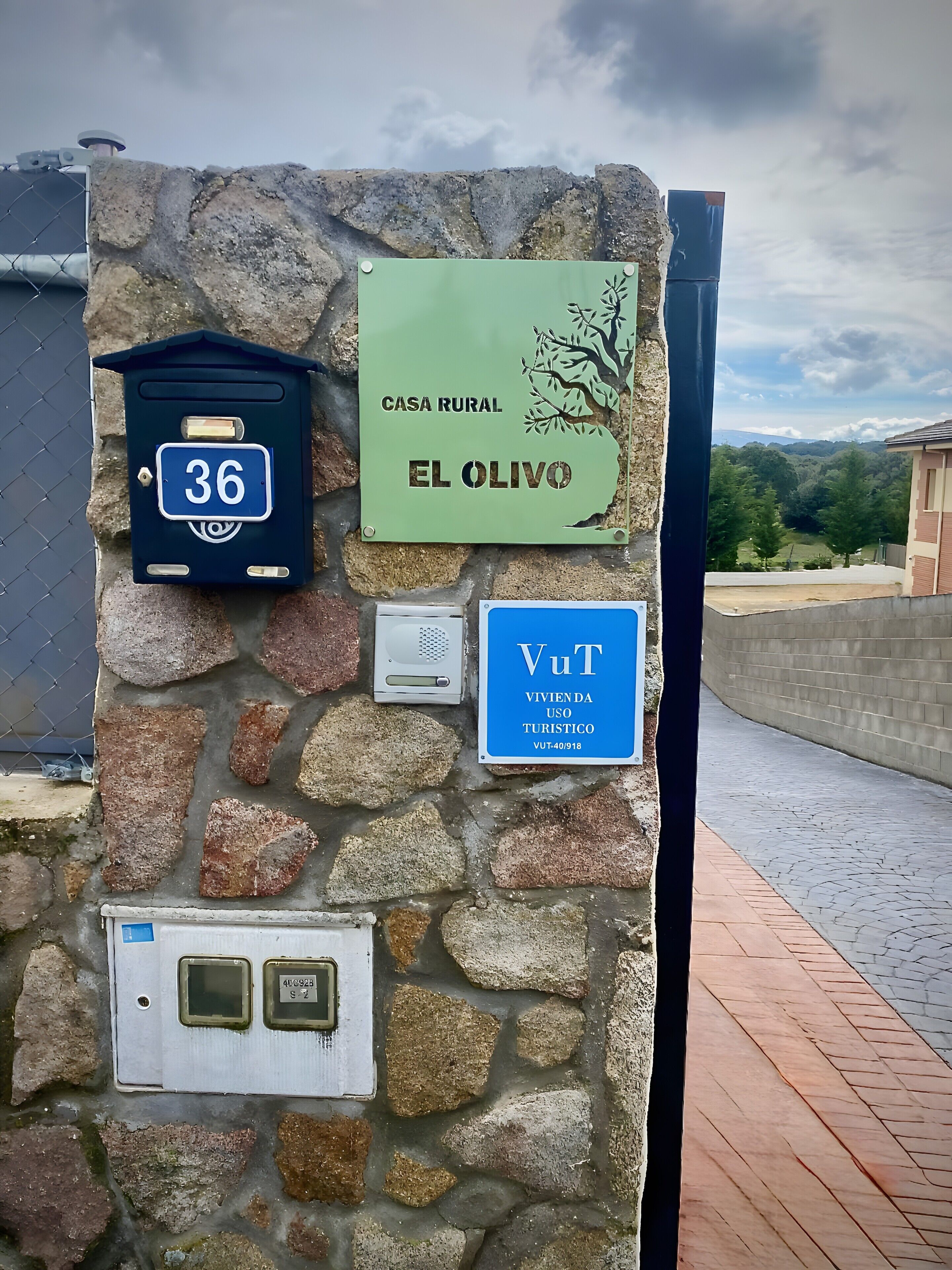 Un muro in pietra con un cartello di casa in stile rustico, una cassetta delle lettere e un armadietto utenze.