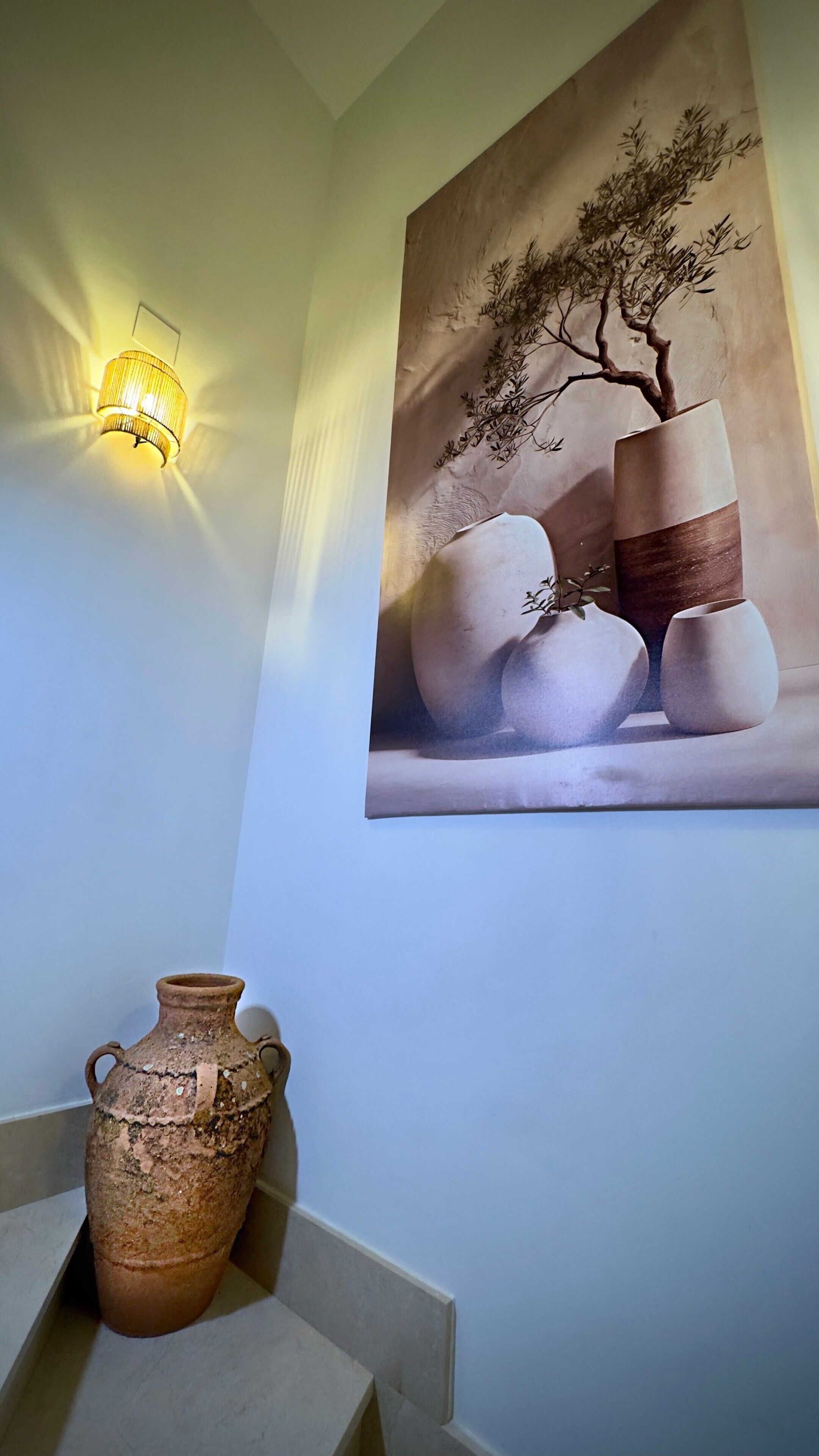 A wall with a textured painting of vases and a wall-mounted light fixture.