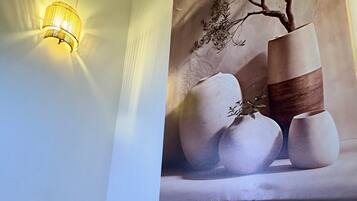 A wall with a textured painting of vases and a wall-mounted light fixture.