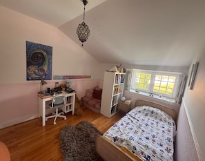 A cozy attic bedroom with a sloped ceiling, a desk with a chair, a bed with a patterned blanket, a bookshelf, and a window with a view. - Family house, garden & pool - sleeps 7 - 5 min surf beach - Lisbon (Carcavelos)