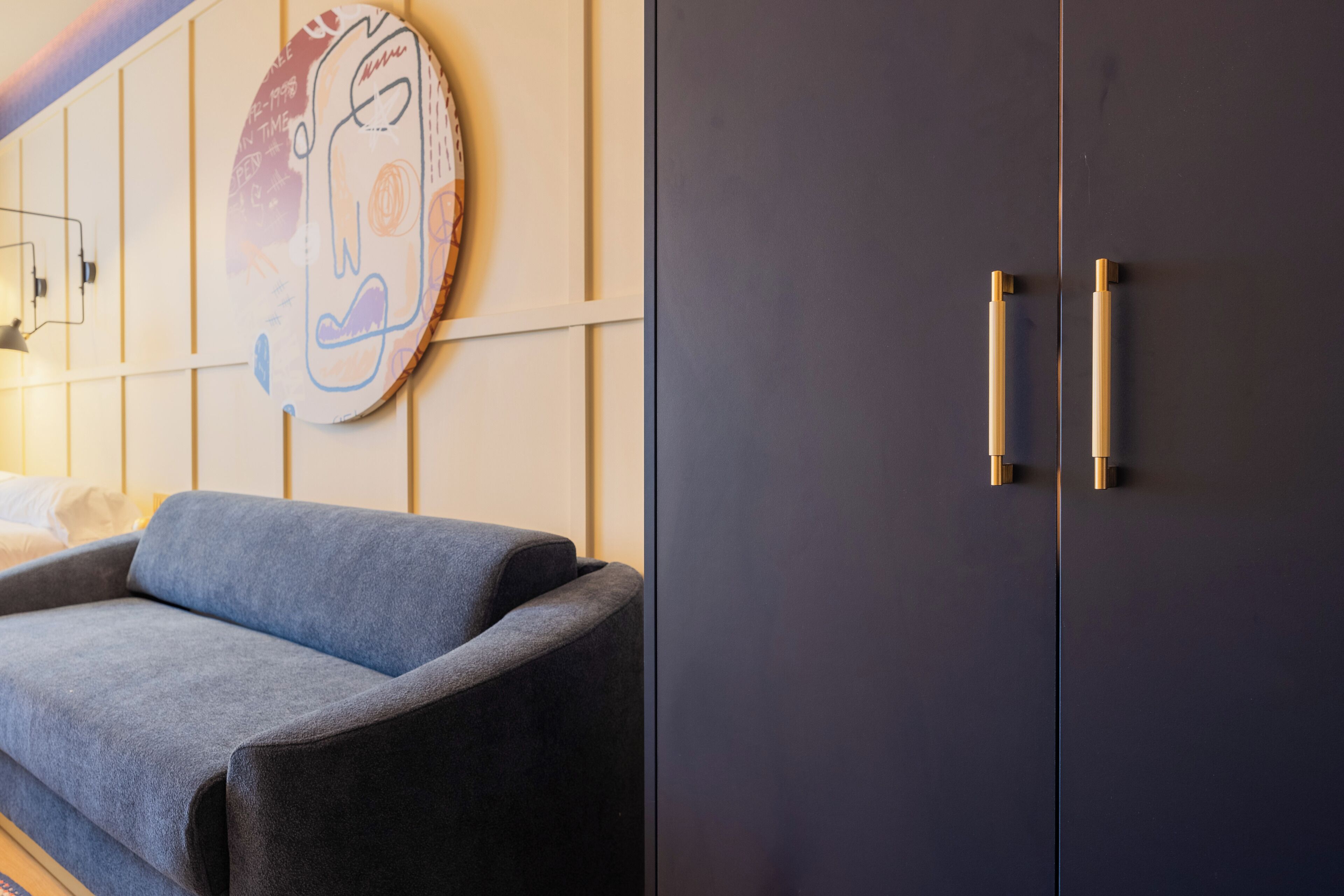 A modern room with a grey sofa, a dark cabinet with gold handles, and a wall-mounted artwork.