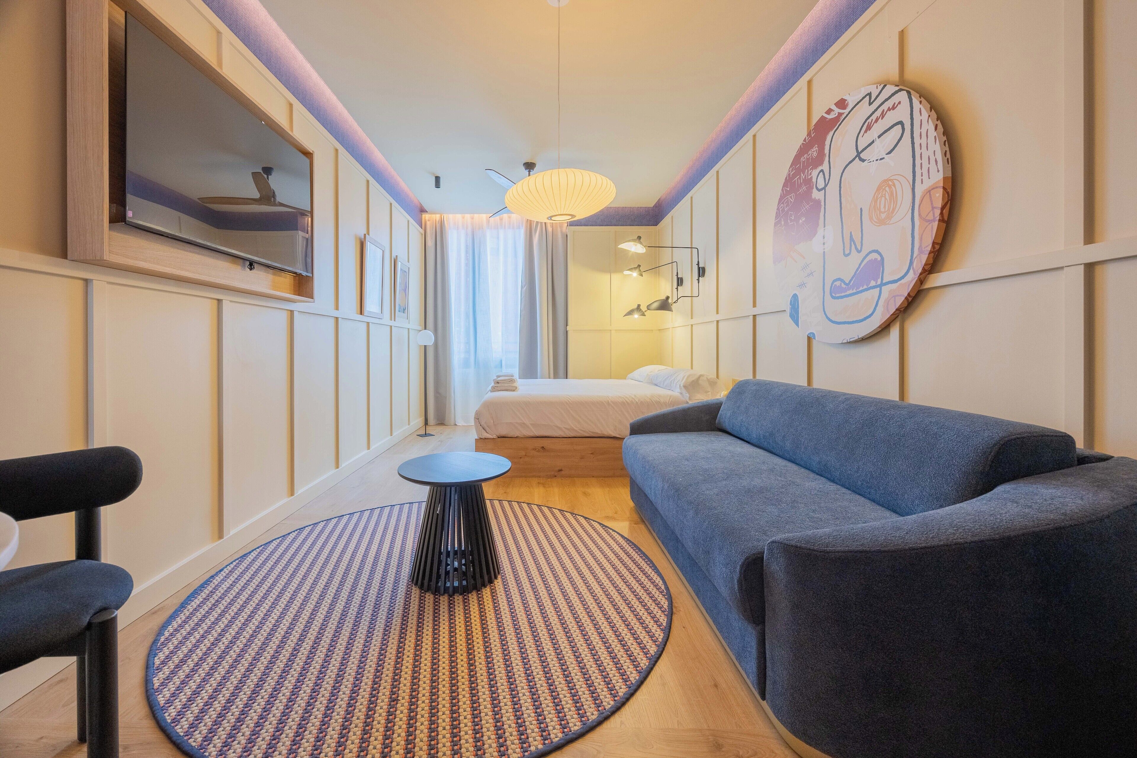 A narrow room with a sofa, a small table, a TV, and a ceiling light.