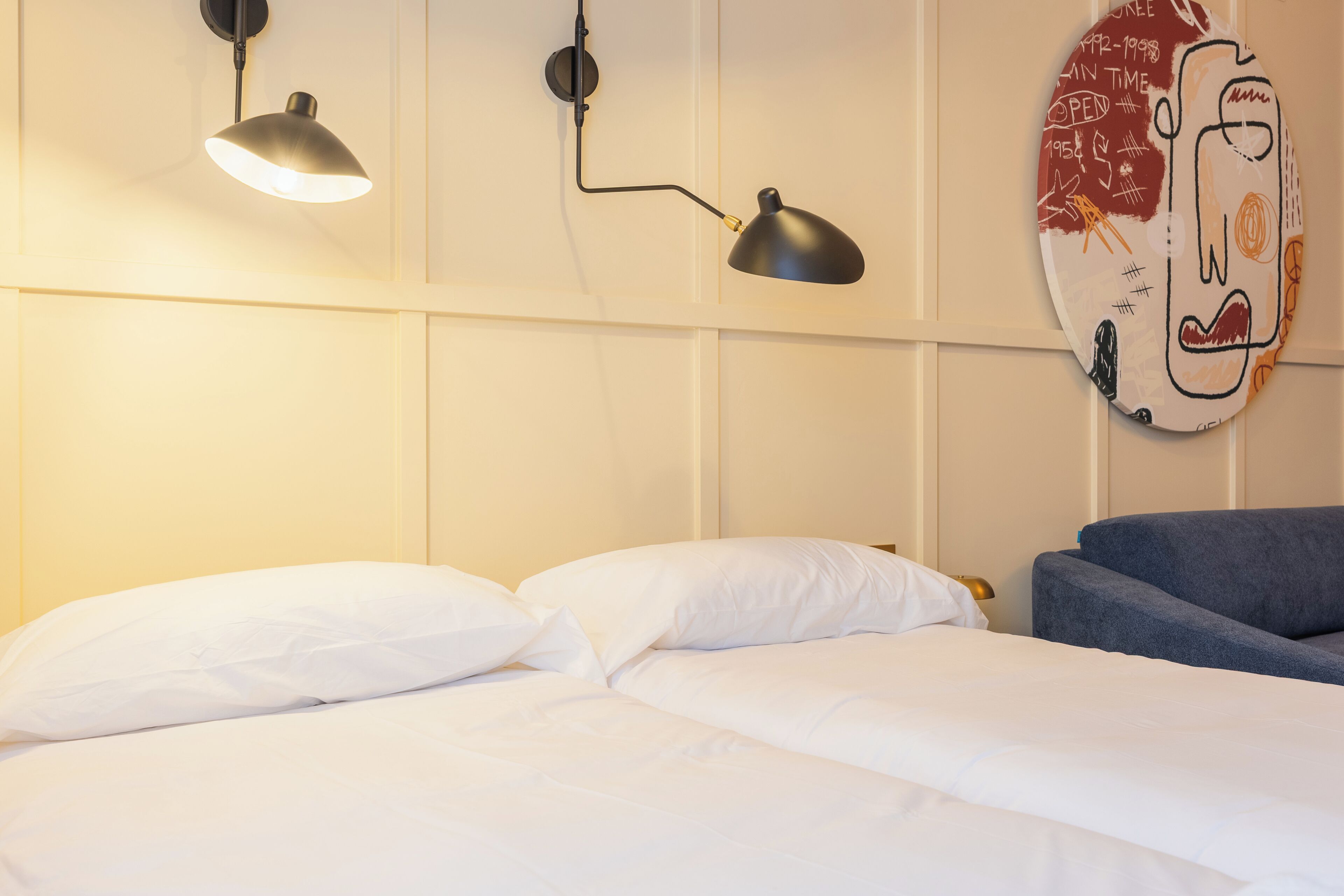 A hotel room with a bed, two wall-mounted lamps, and a wall decoration.