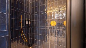 Een hoek van een ruimte met donkerblauwe betegelde muren, een geel douchekop en een goudkleurige douche slang.