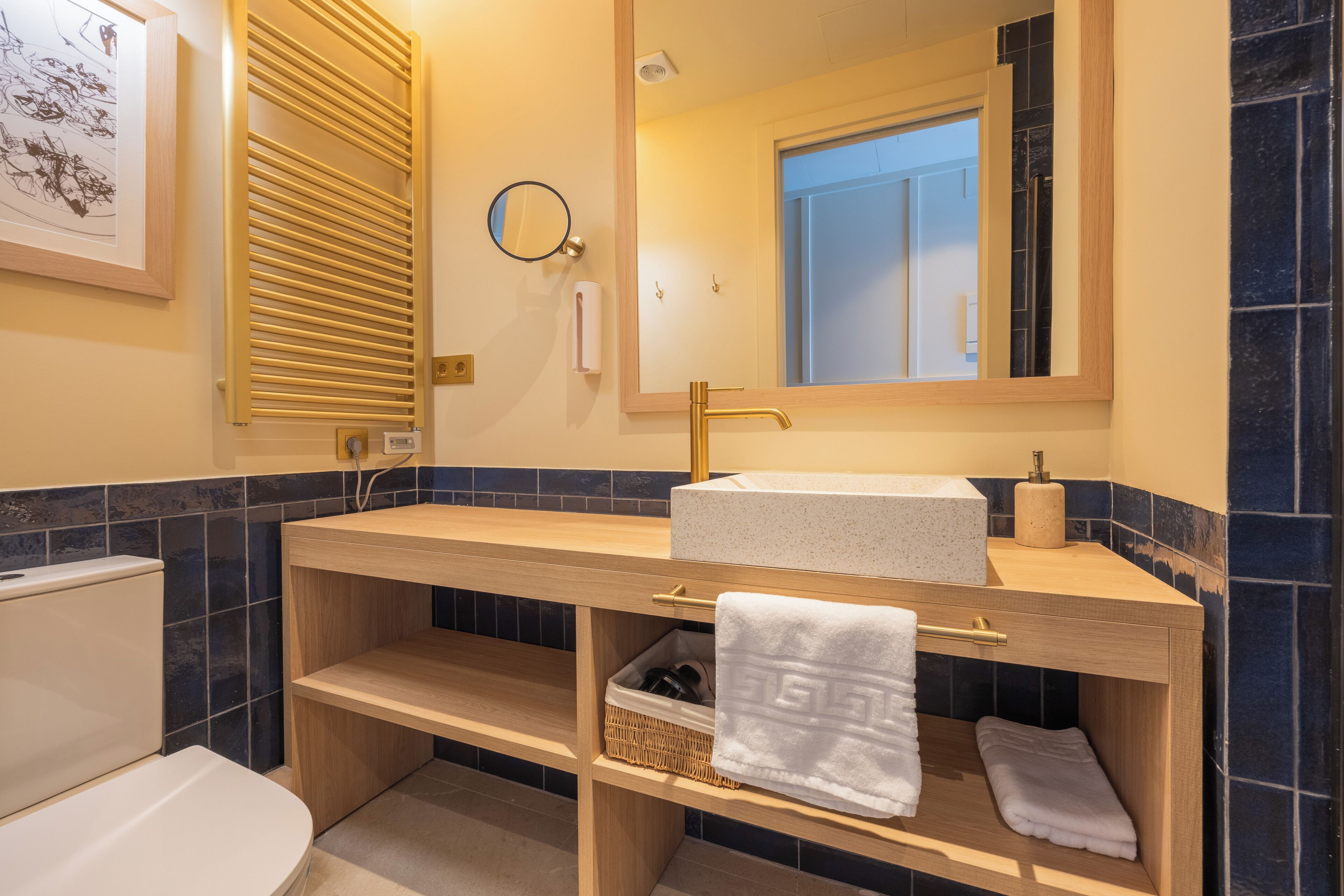 Un baño con tocador de madera, un lavabo blanco, un espejo, un perchero para toallas y un inodoro.