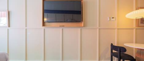 Een moderne kamer met een aan de muur bevestigde televisie, een ronde tafel en een zwarte stoel.