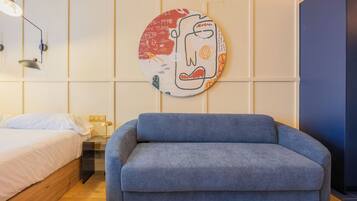 A room with a bed, a blue sofa, a wall-mounted lamp, and a circular artwork.