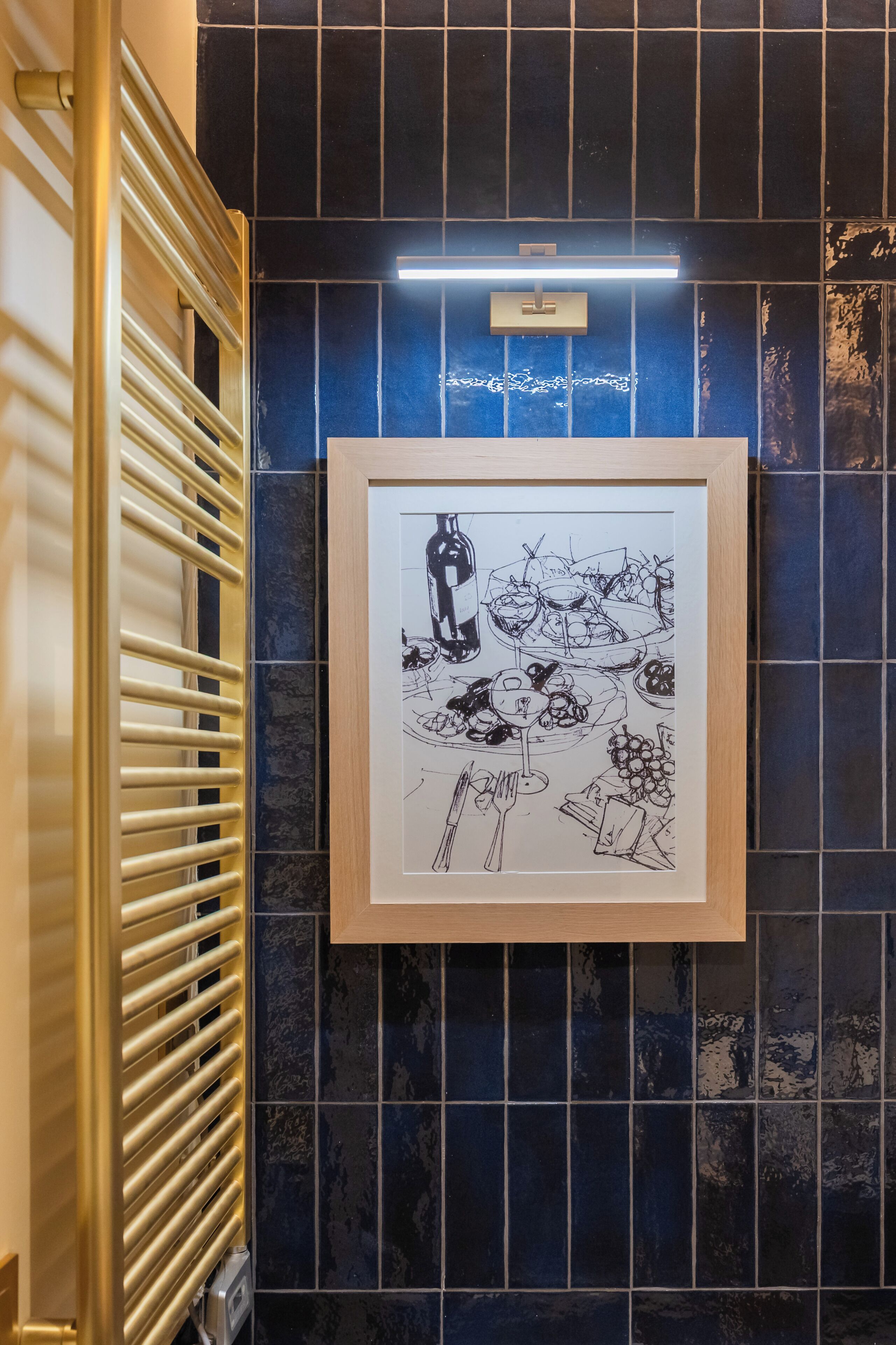 A framed black and white drawing of a dining scene on a tiled wall.