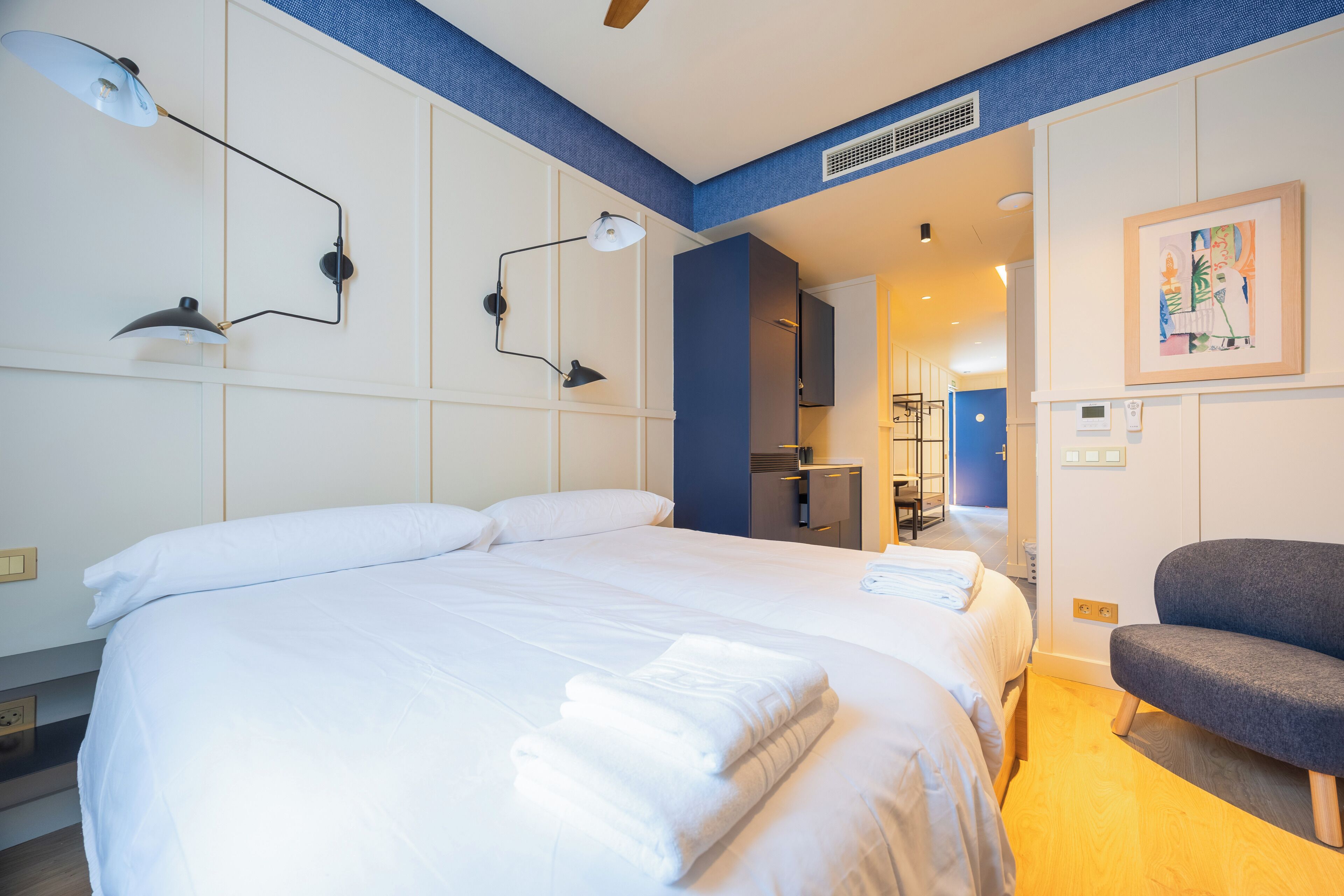 A hotel room with a large bed, two bedside lamps, a chair, and a painting on the wall.