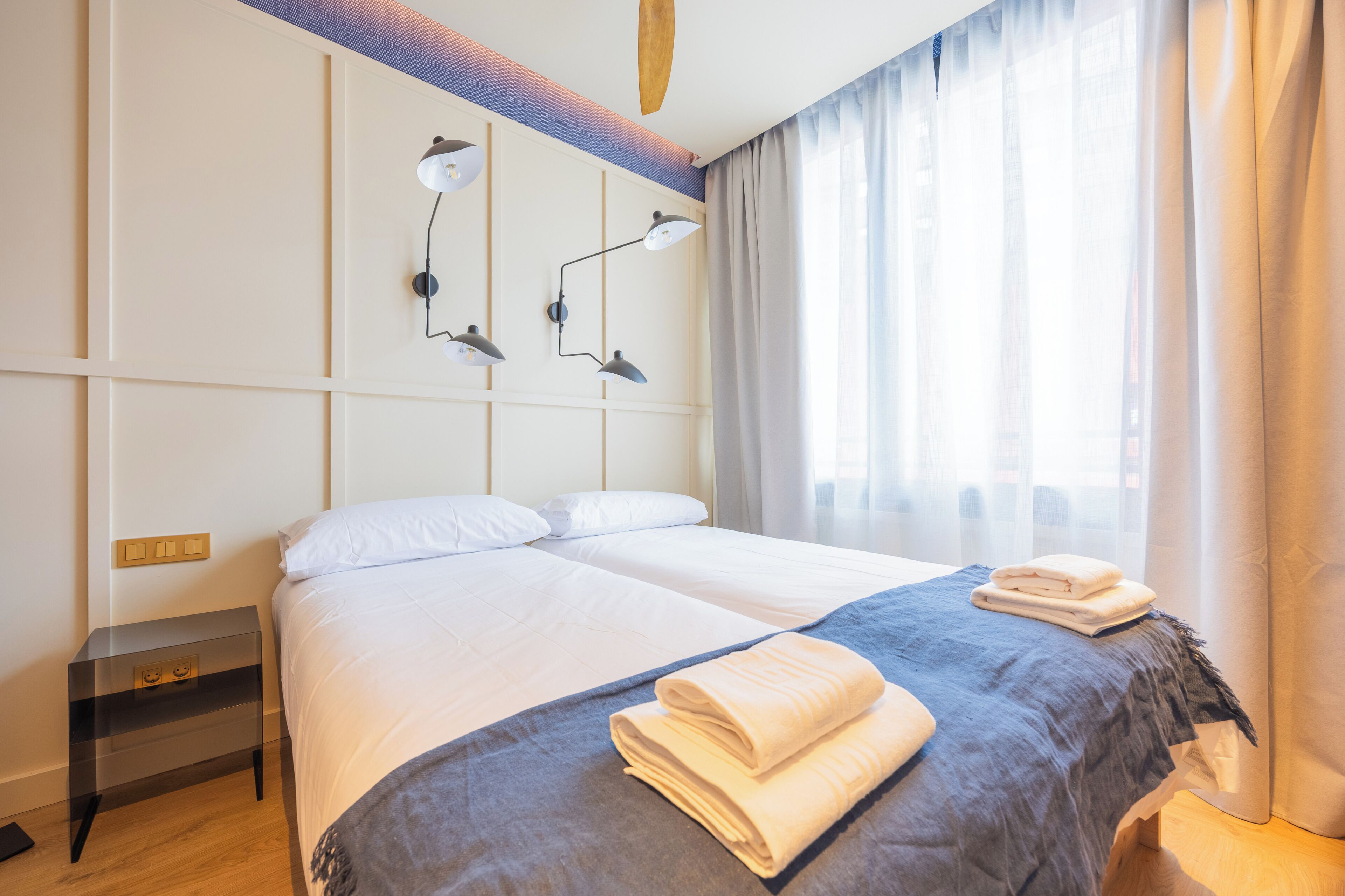 Ein Hotelzimmer mit Bett, zwei Nachttischlampen, einem Nachttisch und einem Fenster mit Vorhängen.