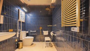 A bathroom with dark blue tiles, a white sink, a toilet, a shower with a gold showerhead, and a towel rack.