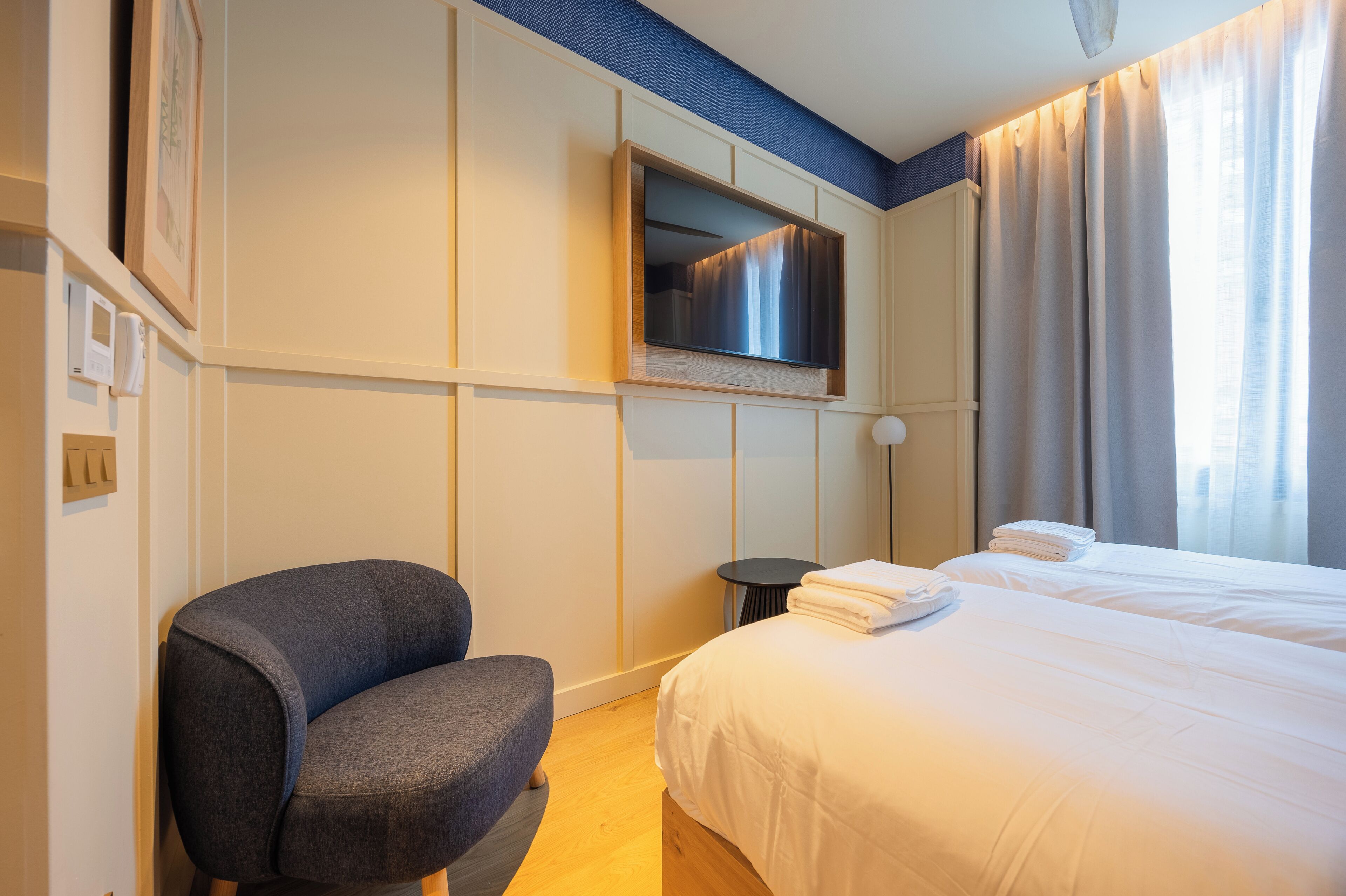 Een hotelkamer met een bed, een stoel, een aan de muur bevestigde televisie en een kleine tafel.