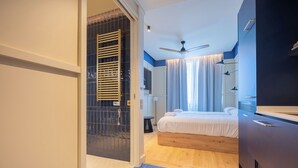 A modern bedroom with a bed, a ceiling fan, and a bathroom with a shower. - CP Apartments Bilbao (Bilbao)