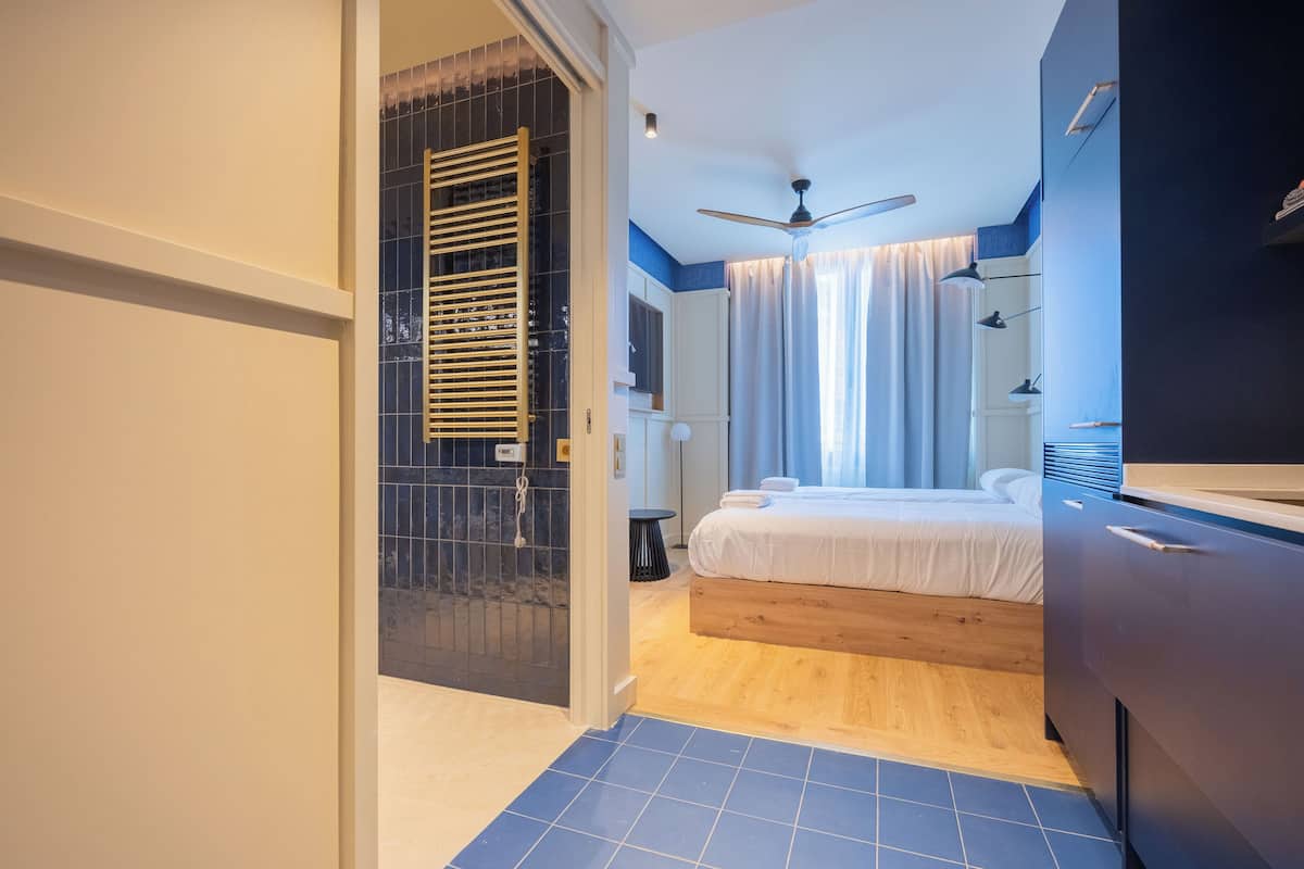 A modern bedroom with a bed, a ceiling fan, and a bathroom with a shower.