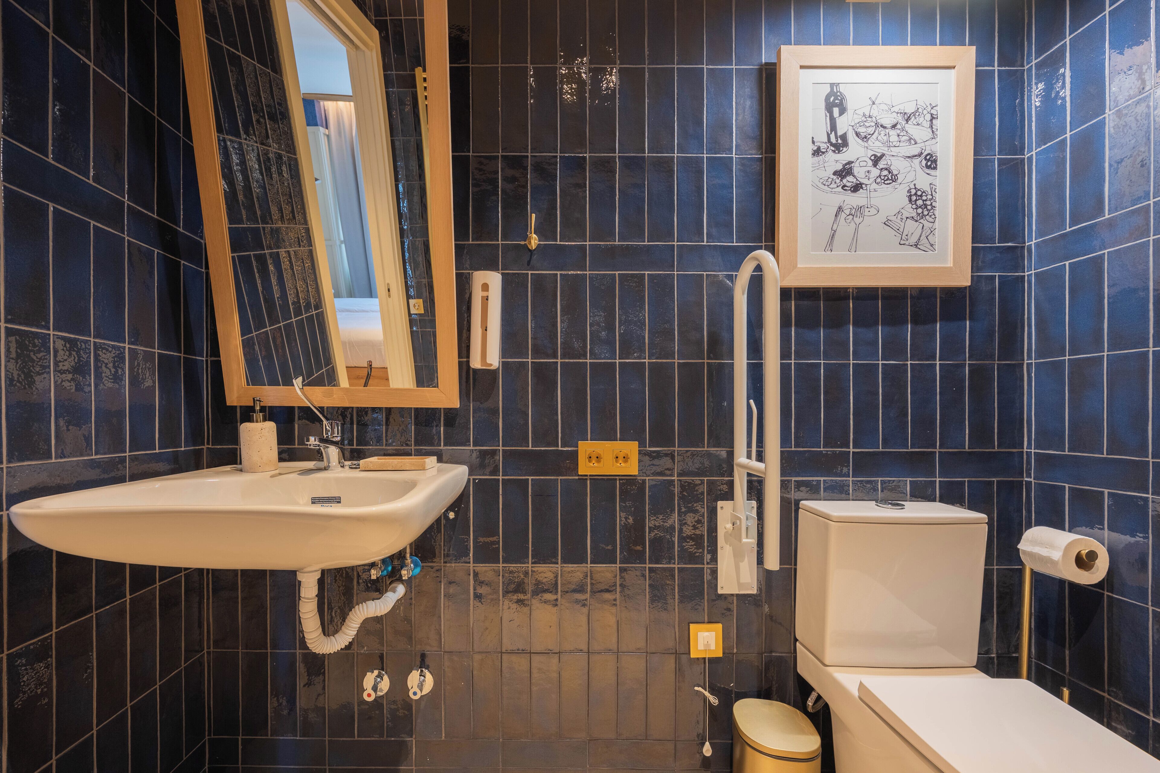 A bathroom with a sink, mirror, toilet, and a framed picture on the wall.