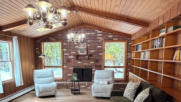 A spacious room with a high ceiling, wooden beams, a fireplace, a bookshelf, and a seating area with a round ottoman and two chairs. - 4BR house in Cheboygan with a game room and a private boat slip nearby (Cheboygan)