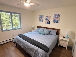A bedroom with a bed, two bedside tables, a ceiling fan, and artwork on the wall. - 4BR house in Cheboygan with a game room and a private boat slip nearby (Cheboygan)