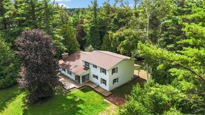 Une maison à deux étages entourée d’une forêt dense.