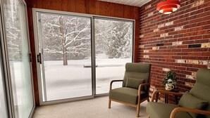 A room with a sliding glass door leading to a snowy outdoor area, a brick wall, and two green chairs. - 4BR house in Cheboygan with a game room and a private boat slip nearby (Cheboygan)