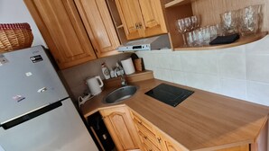 Une cuisine avec des meubles en bois, un évier en acier inoxydable, une bouilloire et un plan de travail surmonté d’un tapis noir.