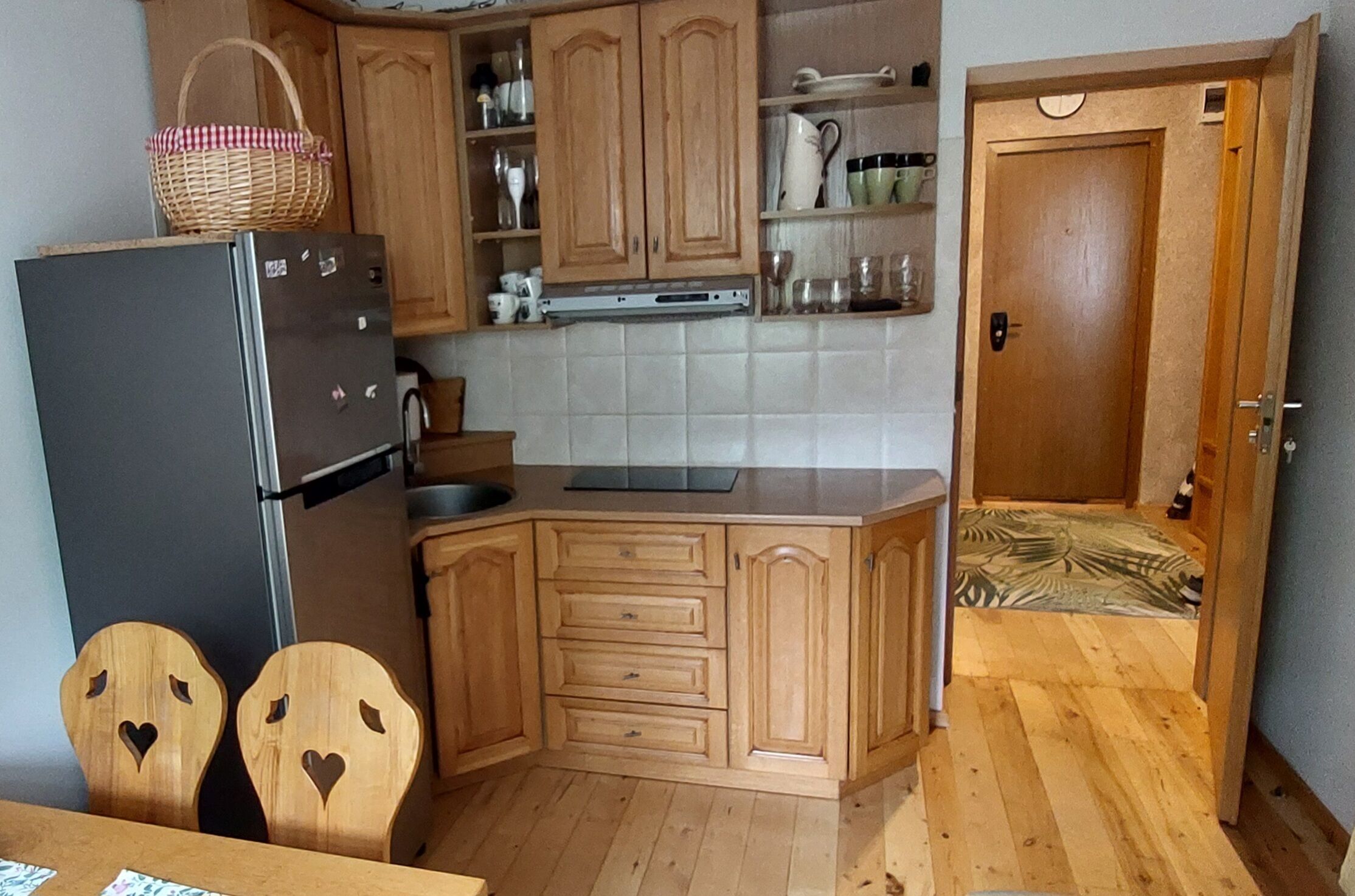 A compact kitchen with wooden cabinets, a refrigerator, a sink, and a dining area with two chairs.